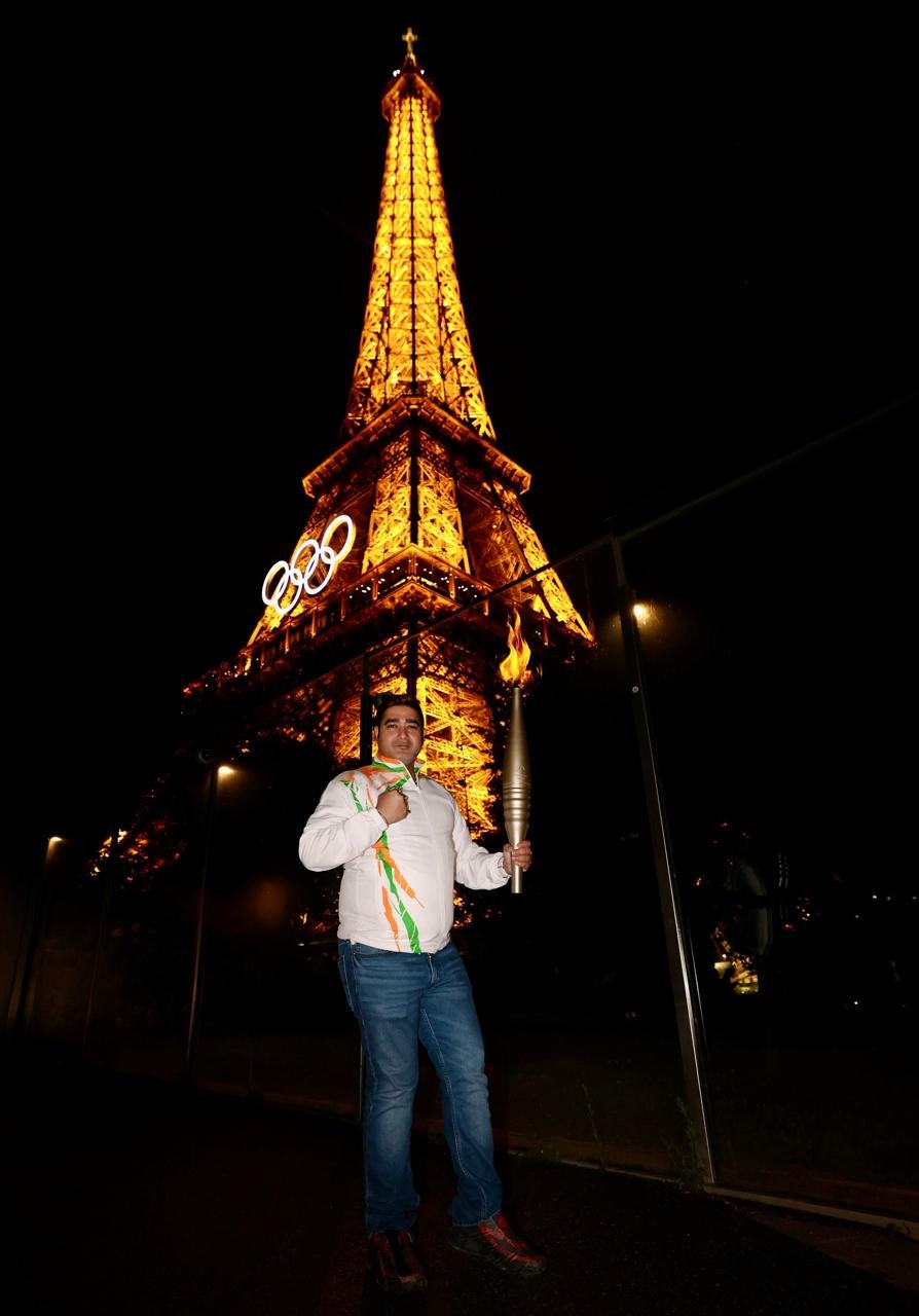 Kunal Saha with the Olympic torch before the Eiffel Tower, as a delegate for the Indian boxing contingent at Paris 2024